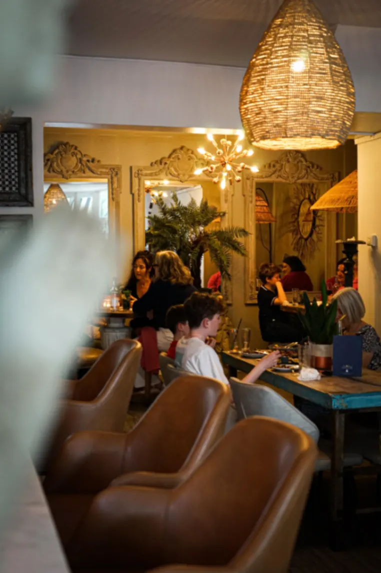 Warmly lit restaurant dining room with leather chairs and ornate mirrors